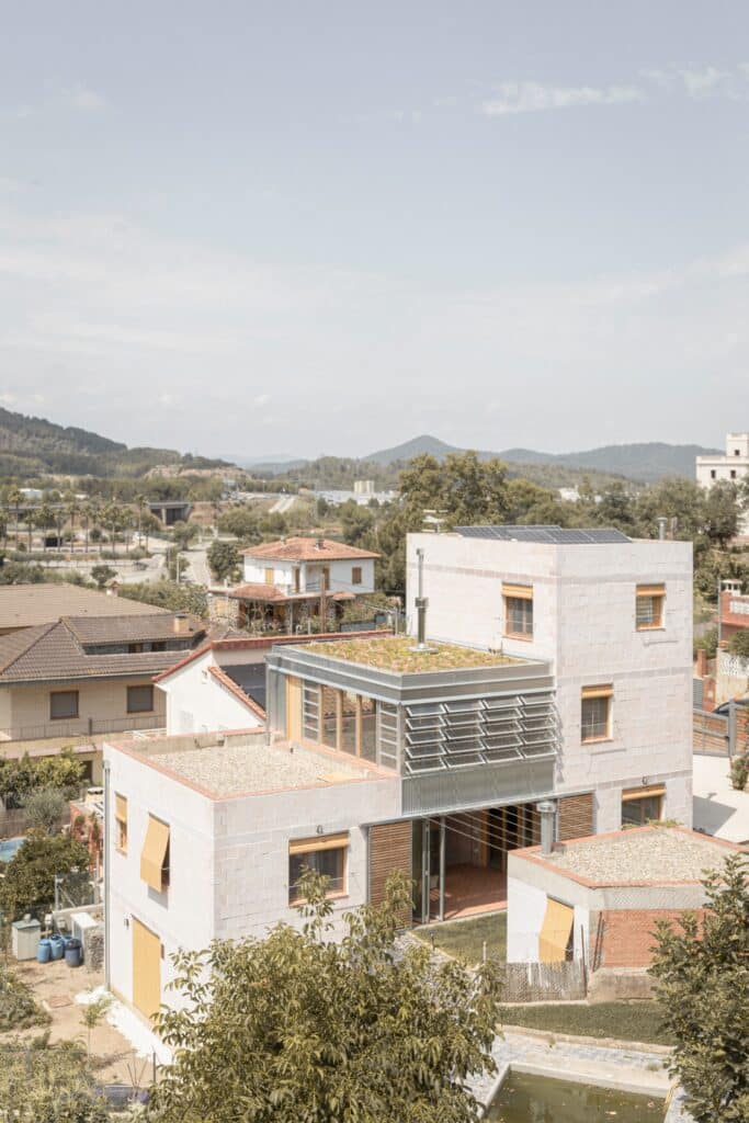 Exterior view of a modern multi-level house on a sloped site with ceramic brick facades, green roofs, and solar panels.