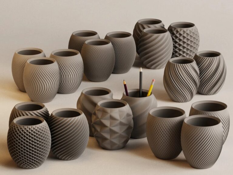 A wide collection of 3D printed grey desk organizers from the Aya and Sfera series featuring various parametric patterns like spiral, wavy, and pinecone textures.