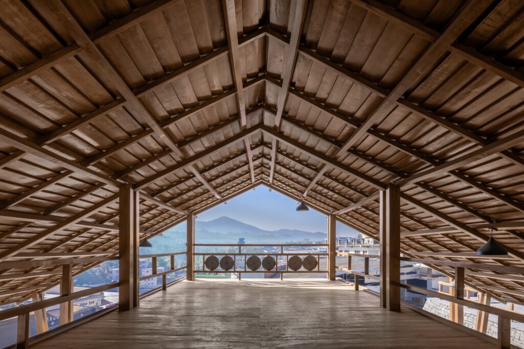 Symmetrical view from under a pitched wooden roof looking out towards the Himalayan mountains through a balcony.