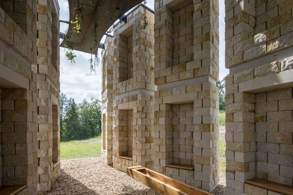 Interior view of the Open Chapel showing wooden seating niches within sandstone pillars and wood chip flooring.