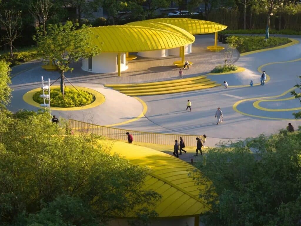 High-angle view of Orchestra Park in Kunshan featuring leaf-shaped yellow pavilions and a modern grey playground with curved yellow lines.