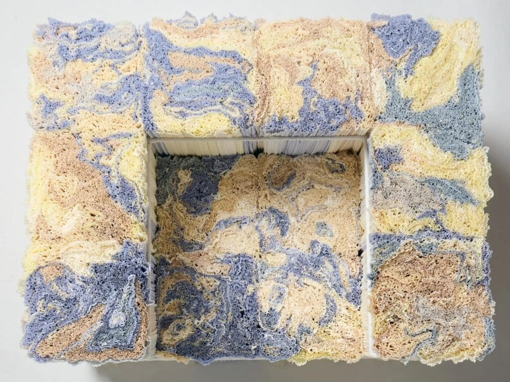 Top view of a rectangular furniture piece made from compressed recycled paper logs with blue and tan marbling patterns.