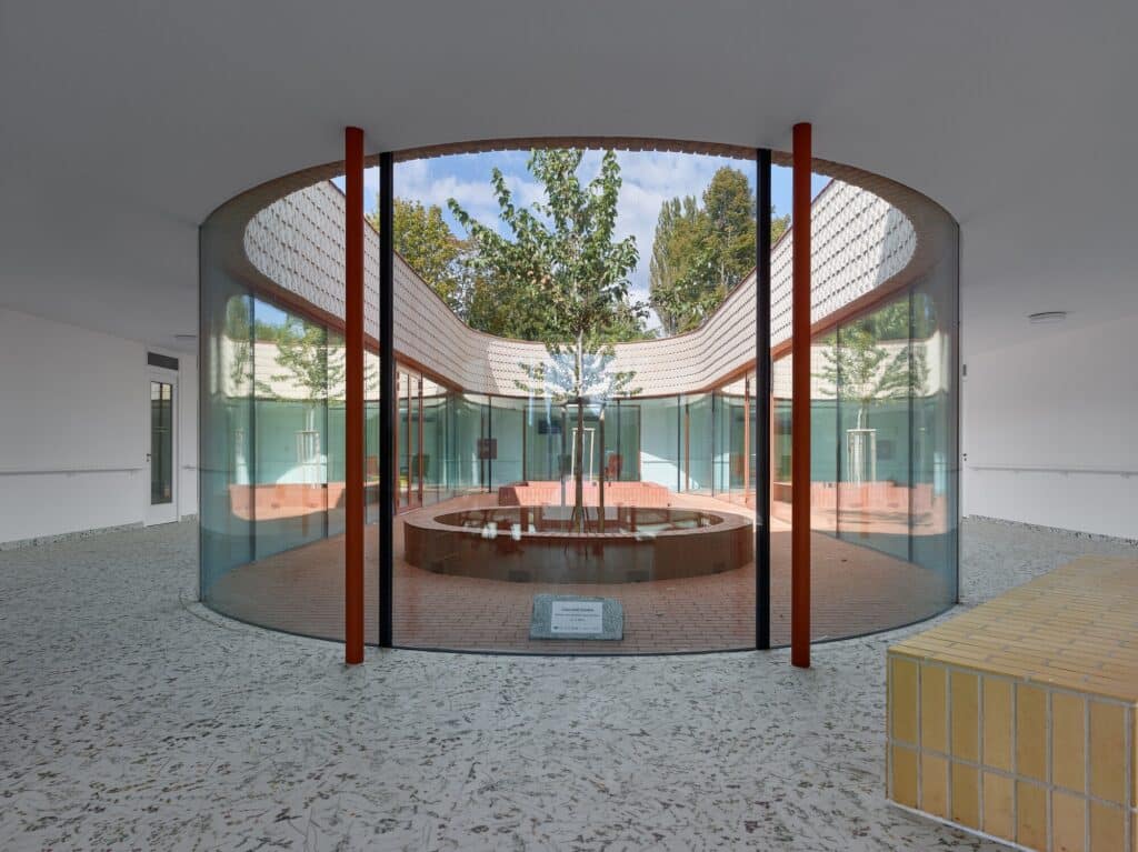 Interior view of a central elliptical courtyard with curved glass walls and a central tree.