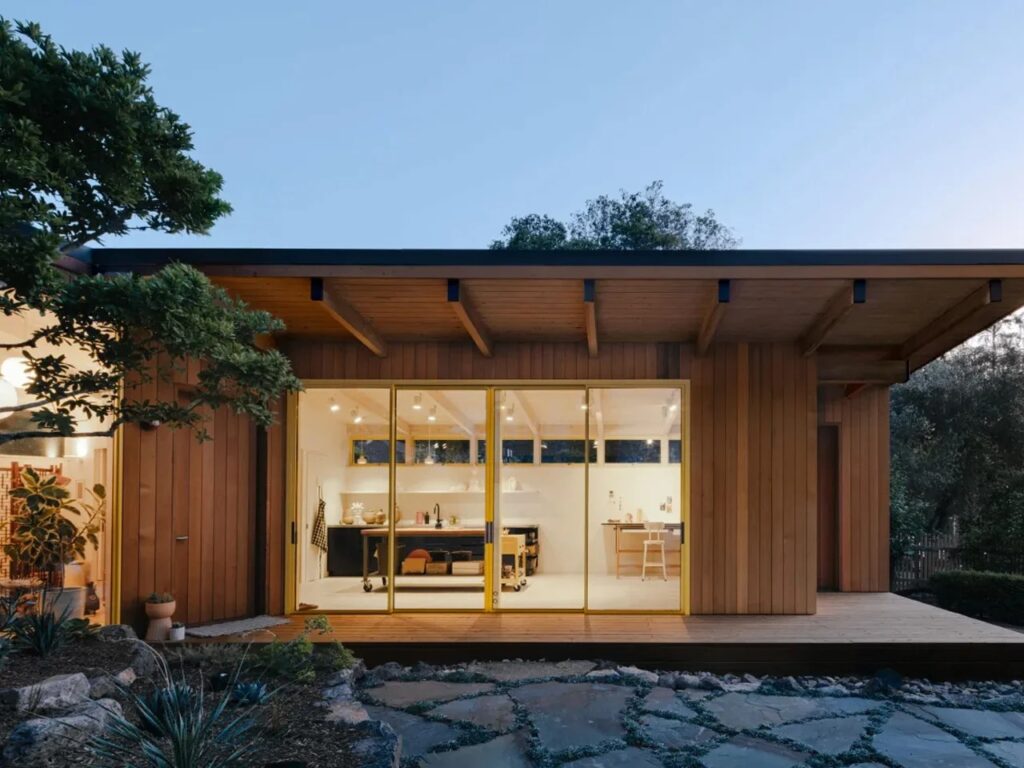Exterior dusk view of Two-Fold Studio showing the warm interior glow through large sliding glass doors and cedar wood cladding.