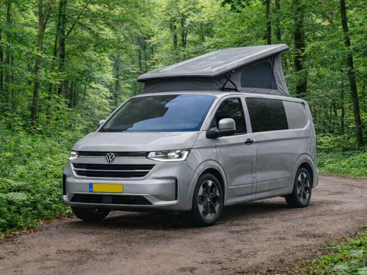 Silver Tonke Baycamper van built on a Volkswagen Transporter chassis parked on a forest dirt road with its pop-up roof extended.