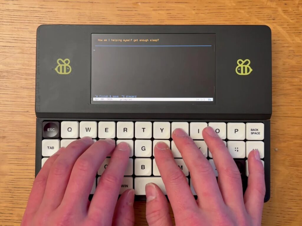 Close-up of a user's hands typing on the mechanical keyboard of the Bee Write Back device with a distraction-free prompt on screen.