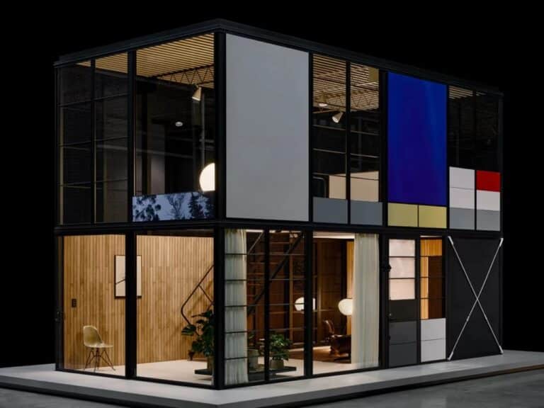 Two-story Eames Pavilion System structure with black aluminum frame, colored panels, and floor-to-ceiling glass windows at night.