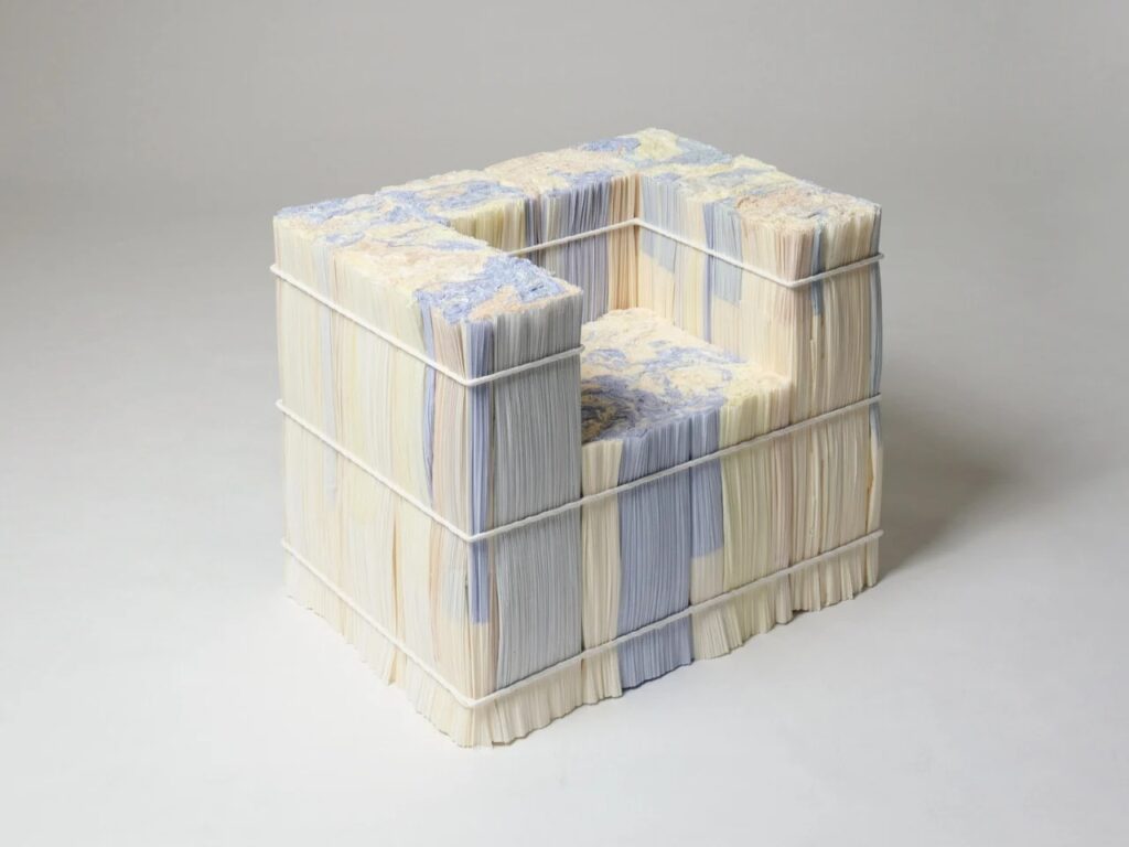 A sculptural armchair designed by Ensamble Studio made from vertical stacks of white and blue pleated paper logs held by metal bands.