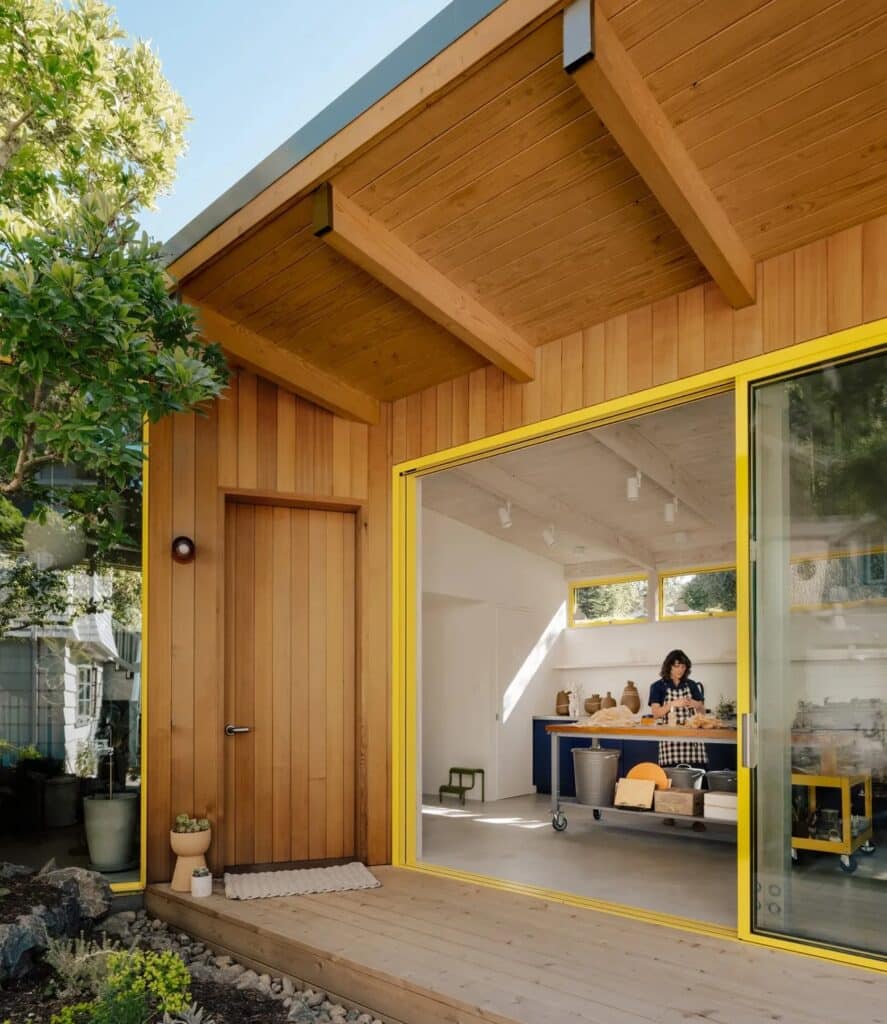 Architect working in a pottery studio with yellow-framed sliding doors and exposed wooden ceiling beams.