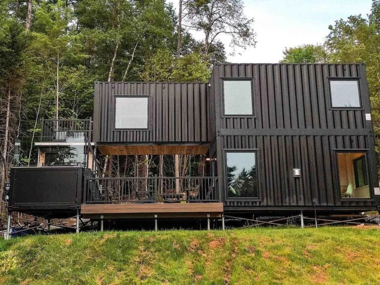 Exterior view of Fairmont Villa, a two-story modern container home with matte black finish and large windows in a forest setting.