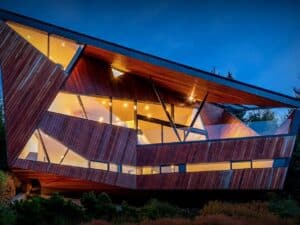 Exterior twilight view of Hadaway House in Whistler featuring its sharp geometric wooden facade and glowing glass windows against a mountain backdrop.