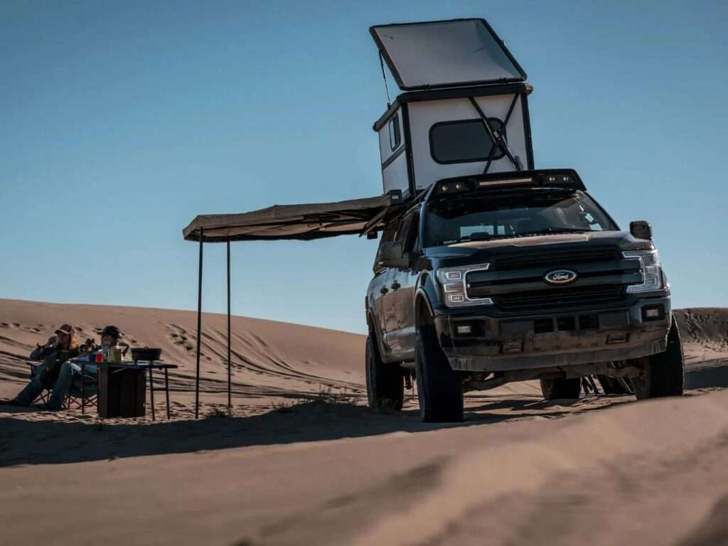 Front view of a Ford F-150 equipped with an Altus hardwall rooftop tent and side awning in a desert environment.