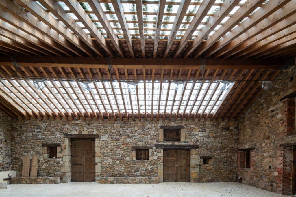Symmetrical view of the wooden beams and glass tile roof with hanging light fixtures against stone walls.