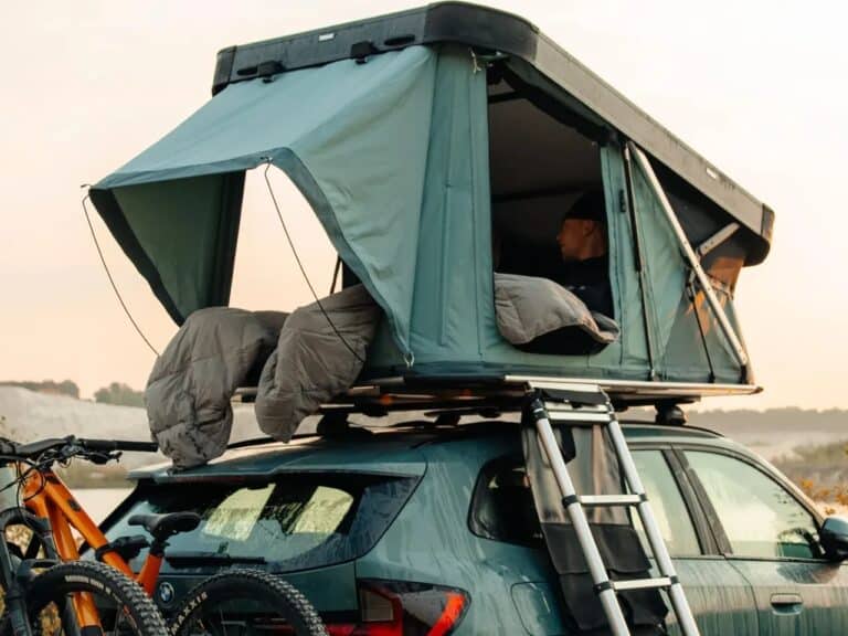 A person inside a Thule Widesky hardshell rooftop tent mounted on a SUV, highlighting the side entrance and telescopic ladder access.