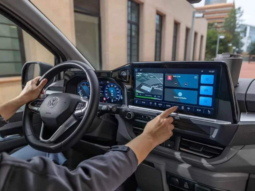 Interior view of the Volkswagen Transporter dashboard showing the digital cockpit and a hand touching the large infotainment touchscreen.