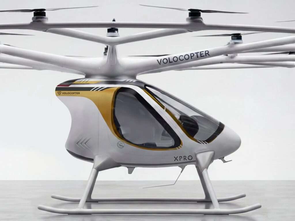 A close-up profile of the white Volocopter VoloXPro cabin, highlighting a distinctive curved gold panel near the roofline, and the 'XPRO' designation on the lower fuselage.