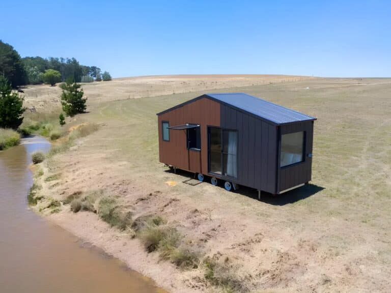 Exterior view of Audrey tiny home by CozyCo featuring wood-textured panels and corrugated aluminum cladding in a rural landscape.
