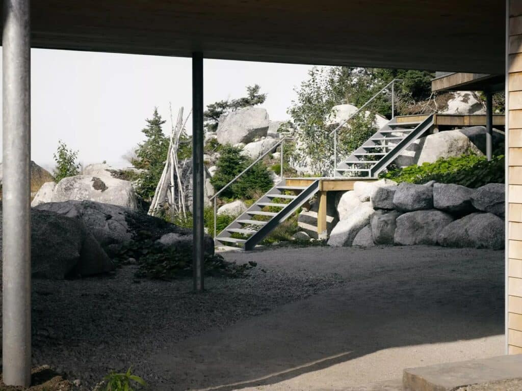 Close-up of the space beneath East River Residence showing slender steel columns and a metal staircase integrated into the rocky terrain.