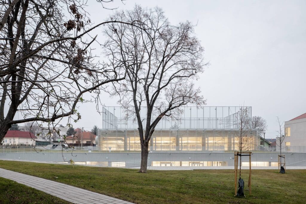 The multipurpose hall at dusk featuring a translucent industrial facade and underground connection.