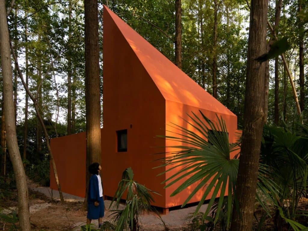 Vertical low-angle shot of the Red Bridge Cabin featuring a sharp, asymmetrical pointed roof rising among dense forest trees.