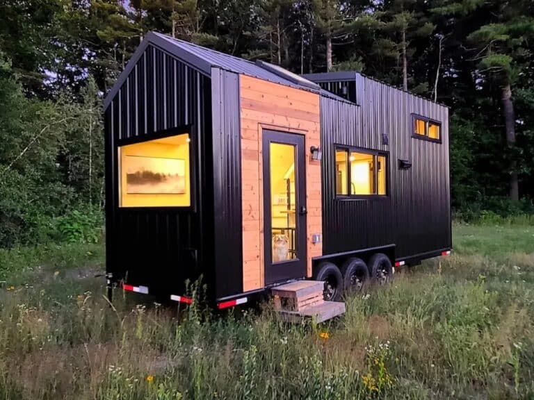 Exterior view of Scandi Inn tiny house featuring black corrugated metal siding and cedar wood accents on a triple-axle trailer.