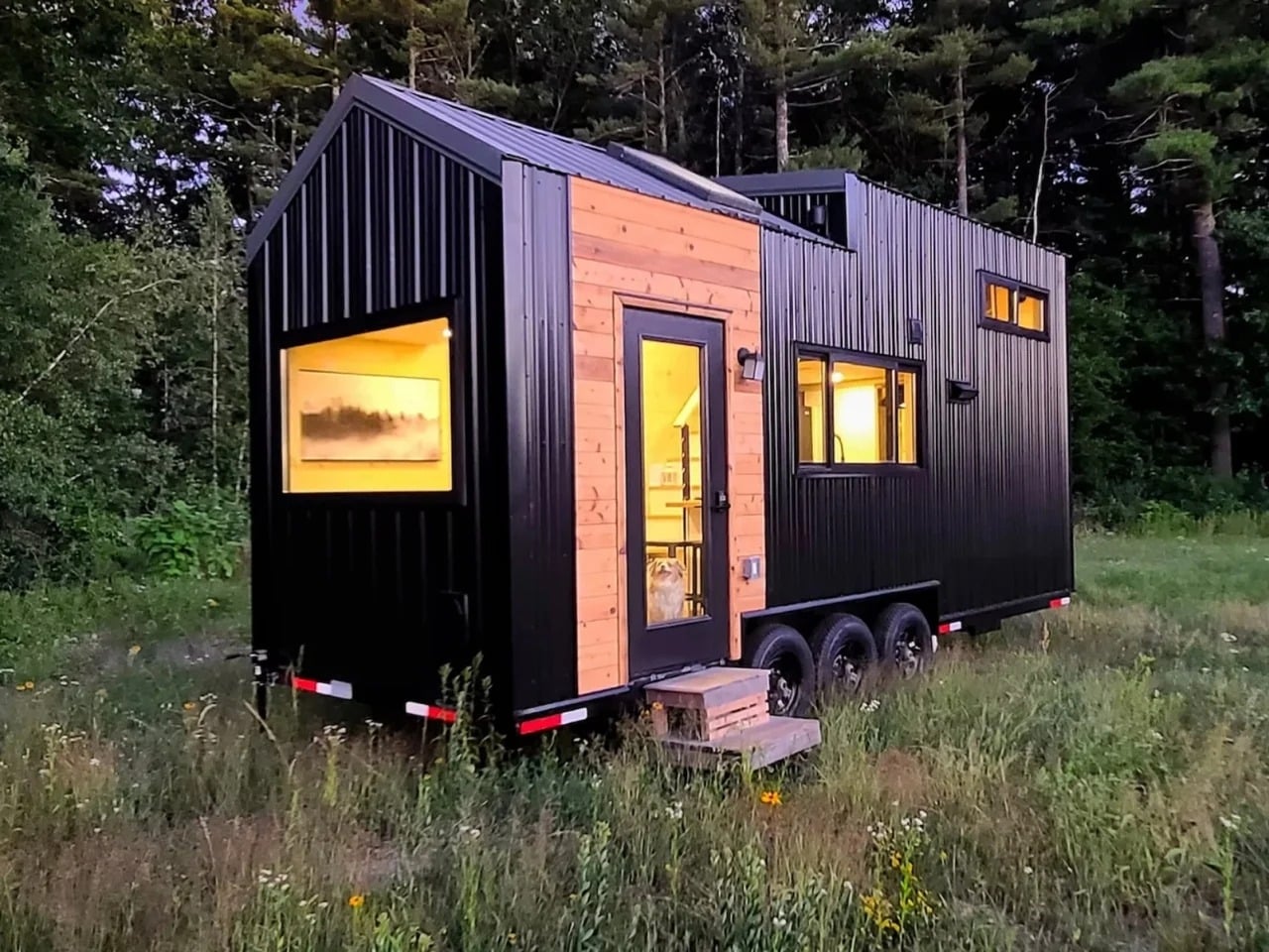 Exterior view of Scandi Inn tiny house featuring black corrugated metal siding and cedar wood accents on a triple-axle trailer.