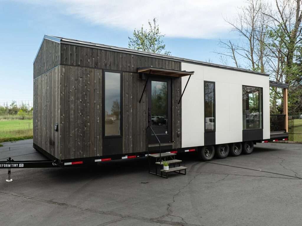 Side profile of Urban Gable Park tiny house with dark wood cladding and white panels on a multi-axle trailer.