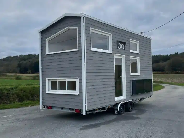 Exterior view of Véronique tiny house with grey spruce wood cladding on a double-axle trailer.