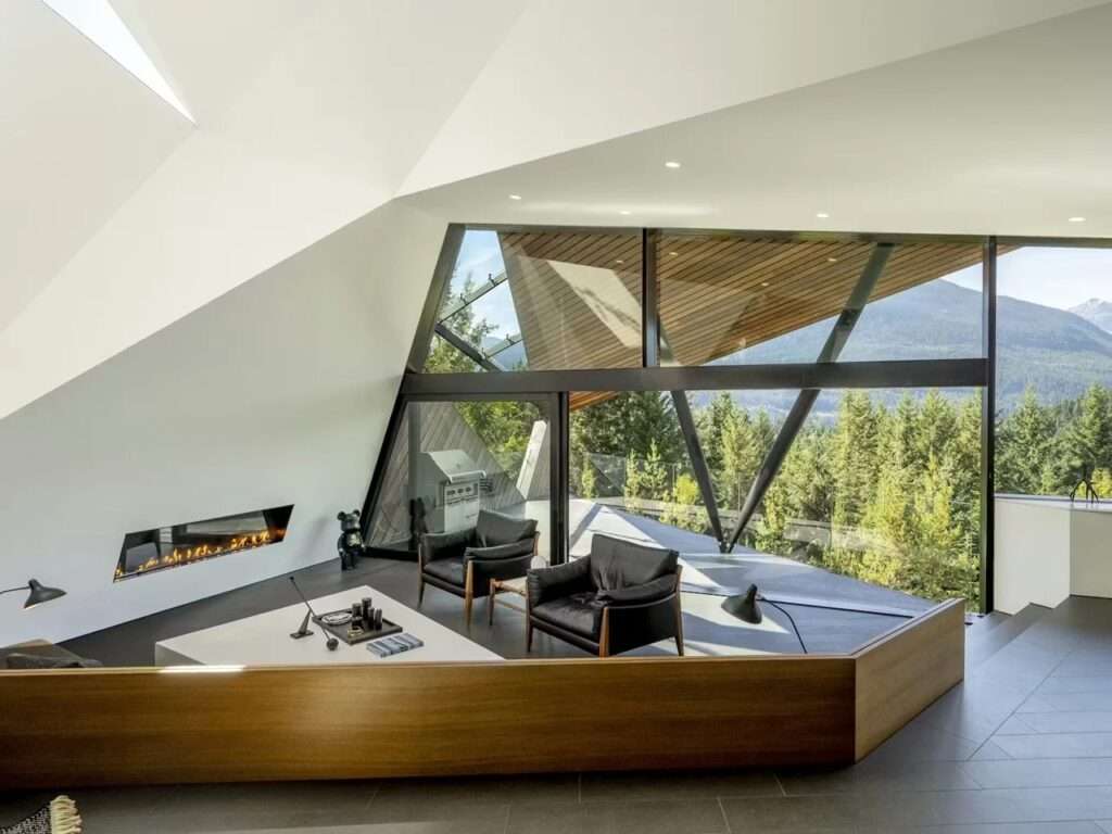 Interior living room of Hadaway House with a modern fireplace, black leather armchairs, and floor-to-ceiling windows overlooking Whistler Valley.