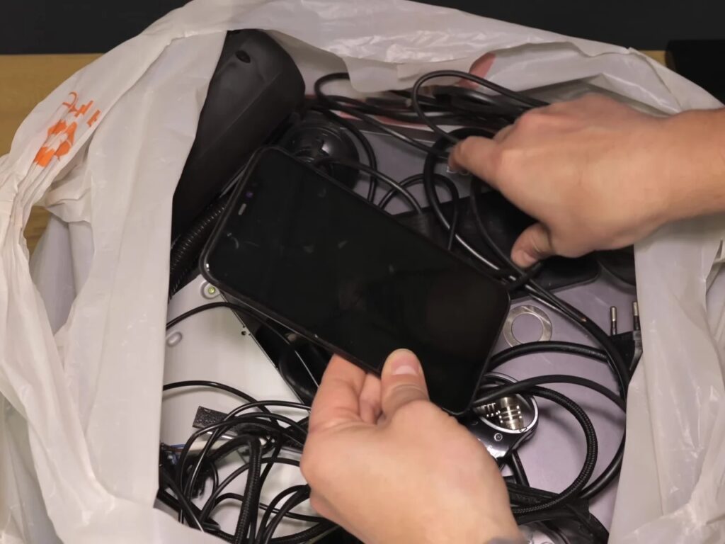 A hand picking an old black Xiaomi Mi 8 smartphone from a pile of electronic waste and cables.