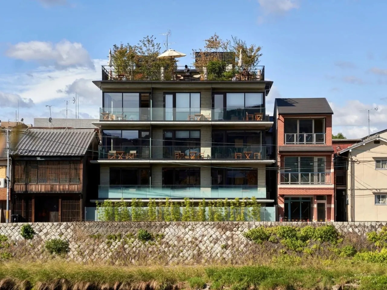 Exterior facade of Genji Kyoto hotel overlooking the Kamo River with rooftop garden and balconies.