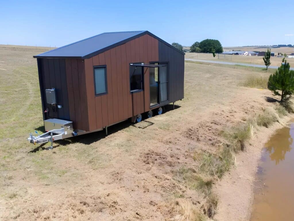 Three-axle trailer base of Audrey tiny house with external storage unit and service connections.