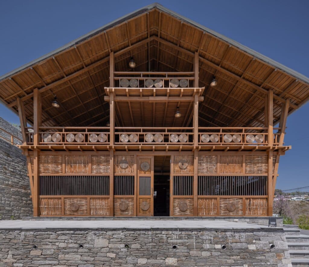Frontal view of the modular wooden facade showing woven bamboo panels and decorative circular craft elements.