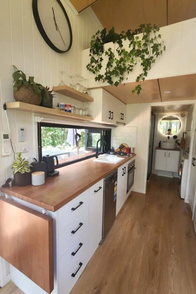Modern tiny home kitchen with wooden countertops, white cabinetry, and a wide horizontal window.