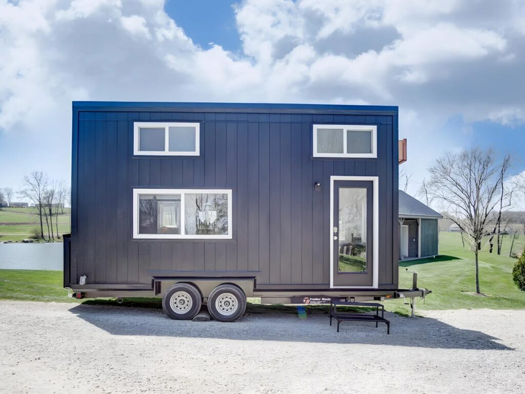 Exterior side view of the Espresso tiny house by Modern Tiny Living on a dual-axle trailer with black engineered wood siding.