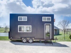 Exterior side view of the Espresso tiny house by Modern Tiny Living on a dual-axle trailer with black engineered wood siding.