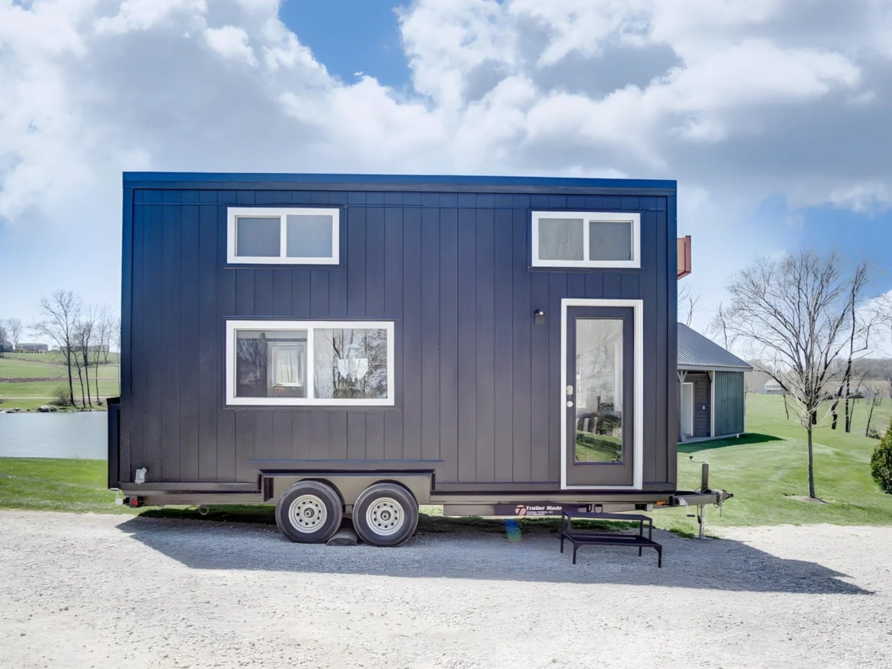 Exterior side view of the Espresso tiny house by Modern Tiny Living on a dual-axle trailer with black engineered wood siding.
