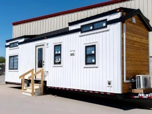 Exterior of Harmony tiny home by Teacup Tiny Homes featuring white vertical siding and natural wood accents on a triple-axle trailer.