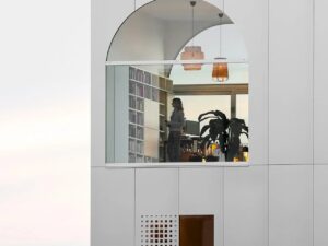 A close-up view of the arched top-floor window of Light House Amsterdam, revealing a modern interior library, bookshelf, and a person standing inside.