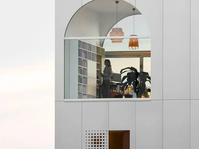 A close-up view of the arched top-floor window of Light House Amsterdam, revealing a modern interior library, bookshelf, and a person standing inside.