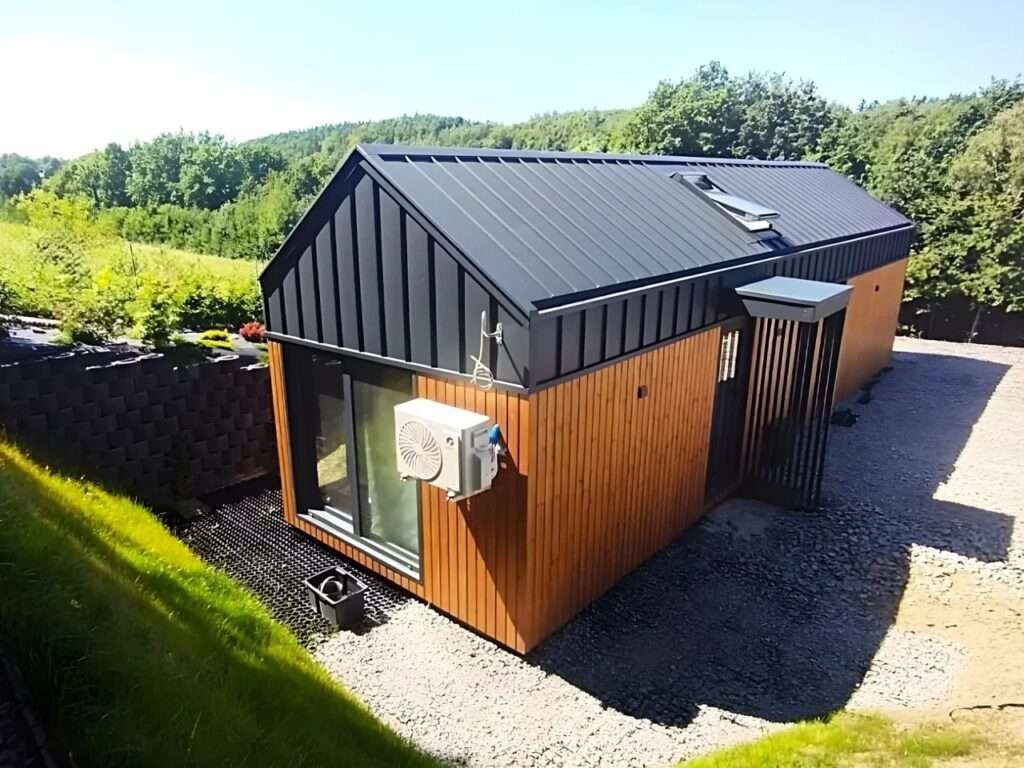 Side perspective of Lox tiny house on a gravel site with an external AC unit and black metal siding.