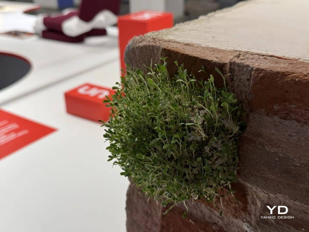 Close-up of a green bio-material unit sprouting from a brick wall crack.