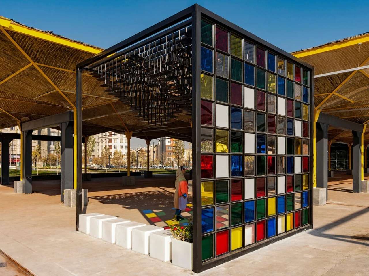 Wide-angle view of the Mirror Pavilion showing the black steel cubic structure with a stained glass grid wall and an undulating mirror ceiling.