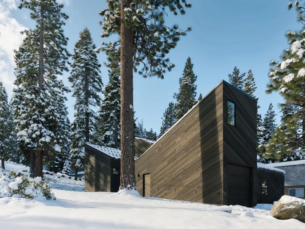 Exterior view of the Staggered Cabin by Mork-Ulnes Architects in Sierra Nevada, showing dark cedar-clad volumes in a snowy pine forest.