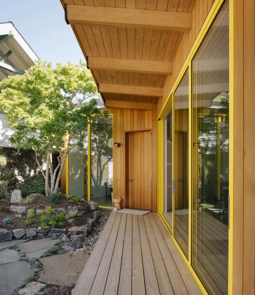 View of the wooden deck and yellow window frames of the L-shaped Two-Fold Studio building.