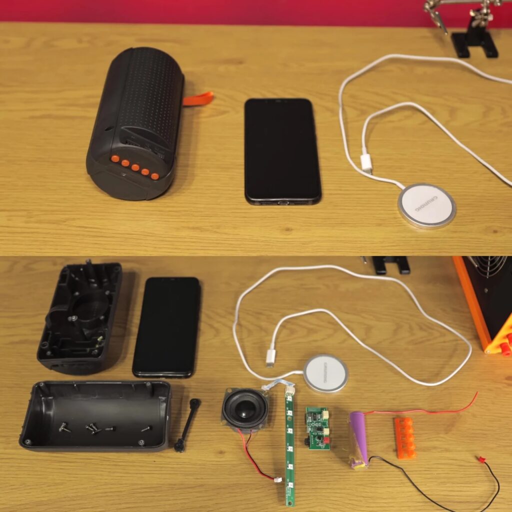 Top view of disassembled electronic components including a smartphone, speakers, wires, and a battery on a wooden desk.