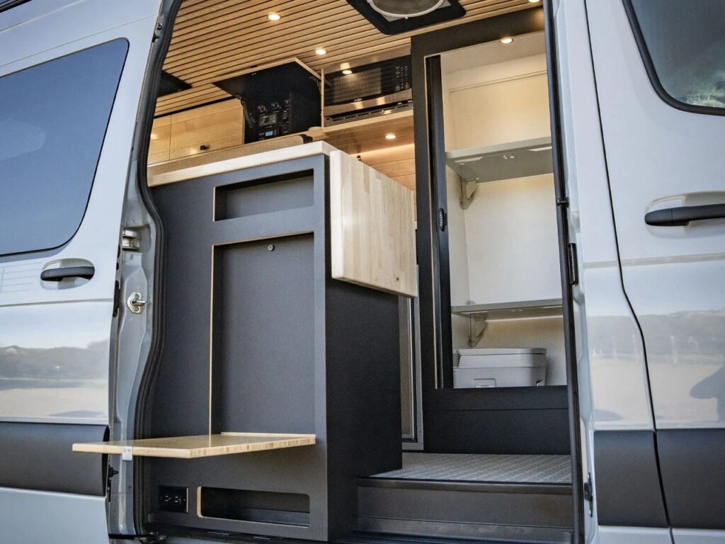 Close-up of the side entrance showing the modular kitchen cabinet and a fold-out bamboo exterior table.