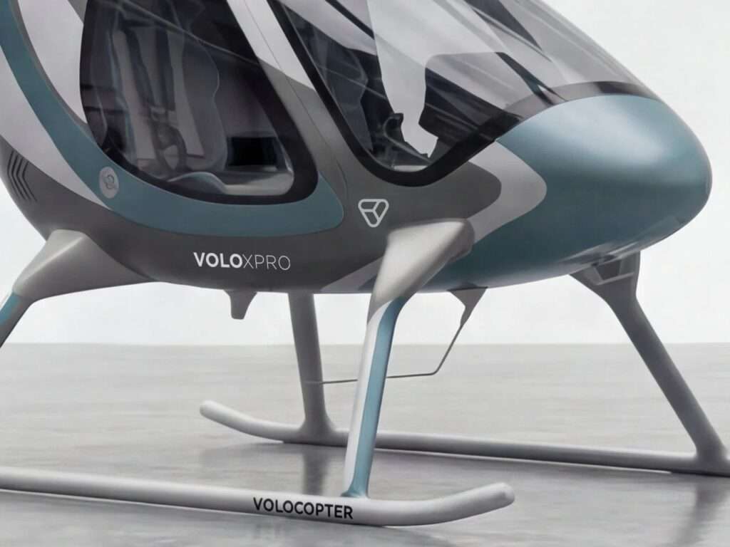 A detail shot focusing on the lower front section of the Volocopter VoloXPro cabin showing the teal-blue nose, the front skid landing gear with 'VOLOCOPTER' branding, and 'VOLOXPRO' text on the fuselage.