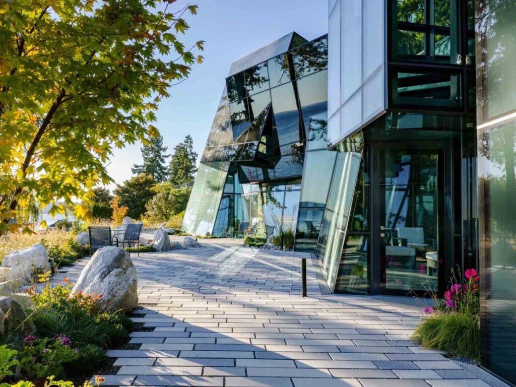 Modern stone pathway leading to the glass entrance of F-House with reflections of the forest on the facade.