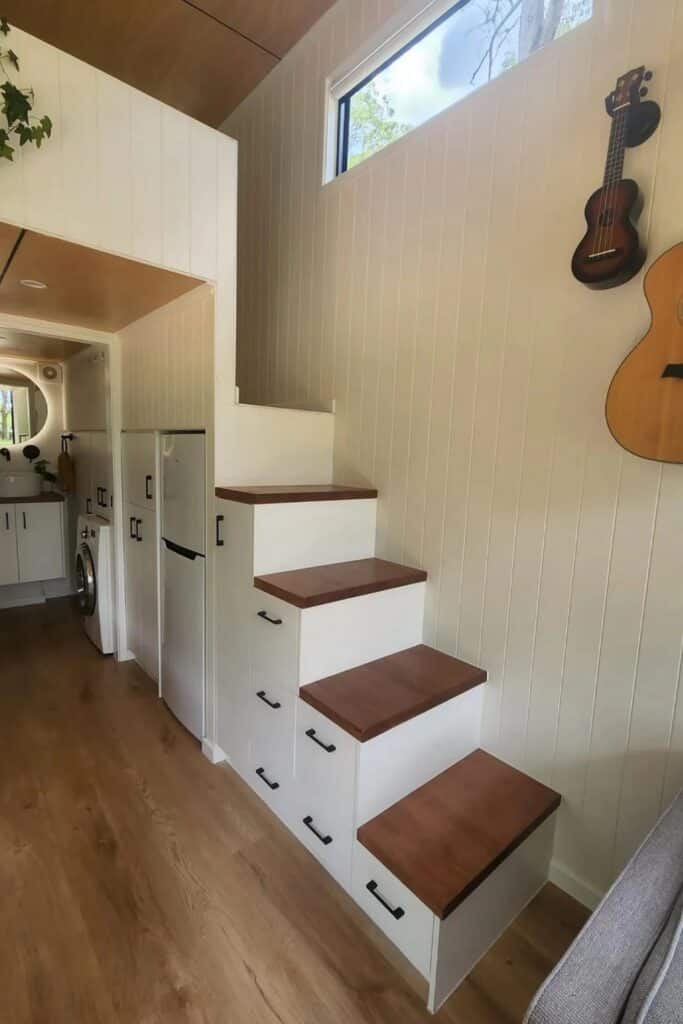 Close-up of white storage stairs with wooden treads in a tiny home interior.